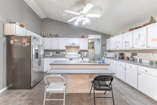 Kitchen with white appliances, under cabinet range hood, a sink, white cabinetry, and high vaulted ceiling | Image 13