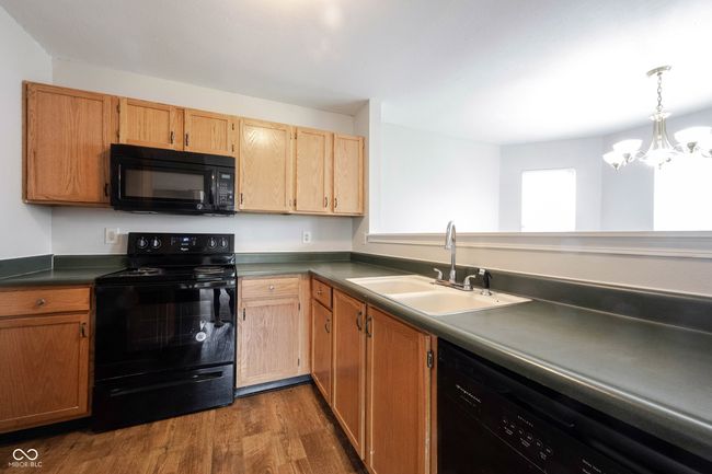 kitchen with dark countertops, wood finished floors, a sink, black appliances, and a notable chandelier | Image 15