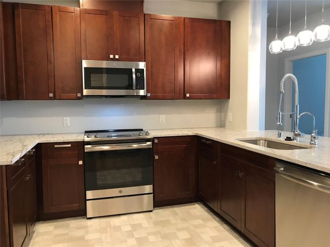Kitchen with appliances with stainless steel finishes, a sink, light stone countertops, light flooring, and hanging light fixtures | Image 4