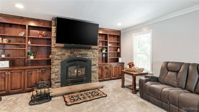 Living room with ornamental molding, a stone fireplace, light carpet. | Image 2