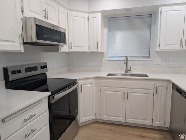 Kitchen with brand new stainless steel appliances, white cabinetry, light countertops, and light wood-style floors | Image 4