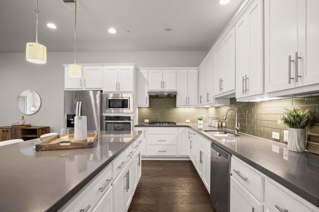 Kitchen with appliances with stainless steel finishes, under cabinet range hood, a sink, dark wood-style floors, and white cabinets | Image 9