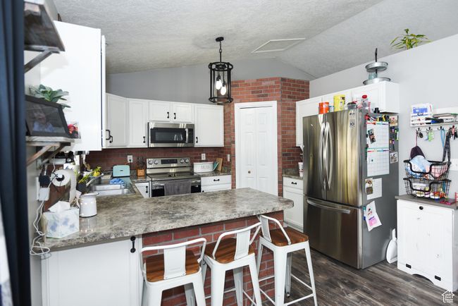 Kitchen featuring a sink, a peninsula, appliances with stainless steel finishes, lofted ceiling, and dark wood finished floors | Image 14