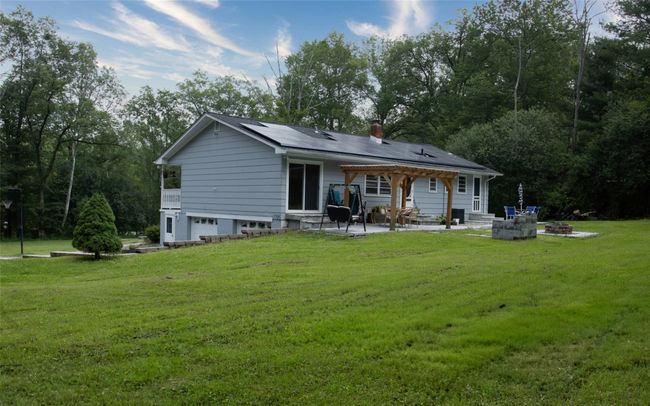 Back of house with a patio, a garage, a lawn, roof mounted solar panels, and a chimney | Image 7