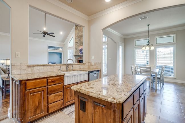 Kitchen with visible vents, a sink, brown cabinetry, stainless steel dishwasher, and light stone counters | Image 13
