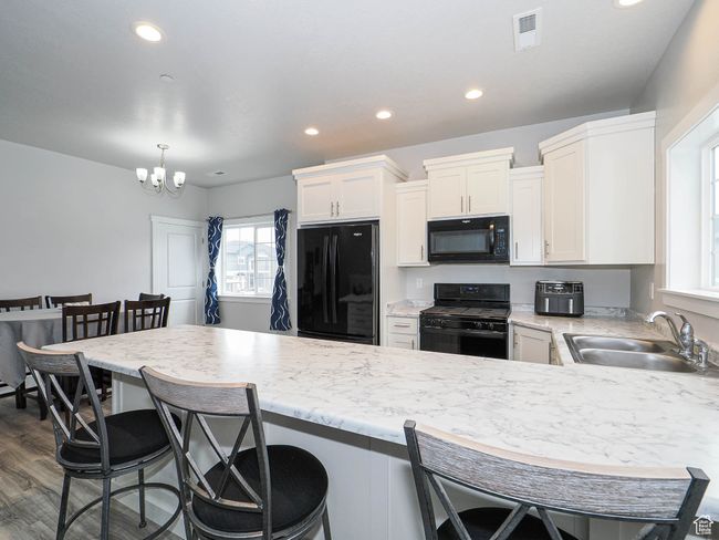 Kitchen with a sink, white cabinetry, a peninsula, visible vents, and black appliances | Image 13