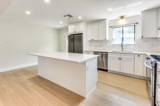 Kitchen featuring decorative backsplash, appliances with stainless steel finishes, a center island, a sink, and visible vents | Image 13
