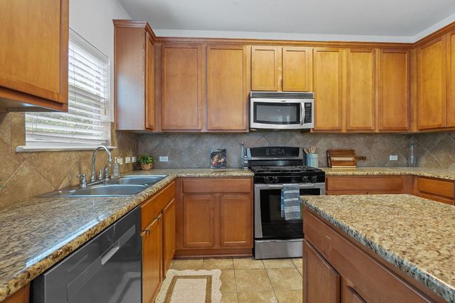Kitchen with stainless steel appliances, a sink, decorative backsplash, brown cabinetry, and light stone counters | Image 12