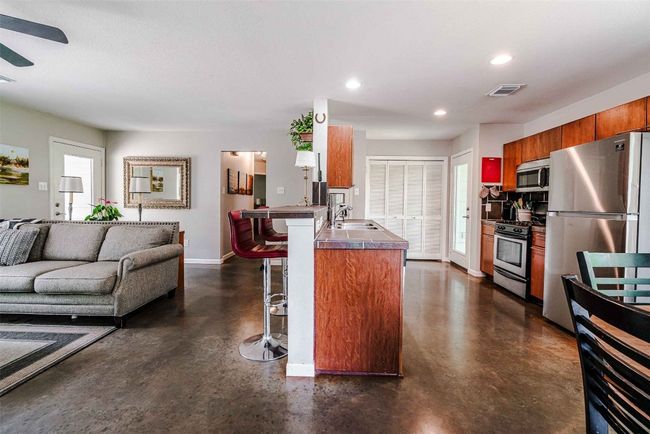 Kitchen featuring appliances with stainless steel finishes, open floor plan, finished concrete floors, a kitchen bar, and visible vents | Image 8