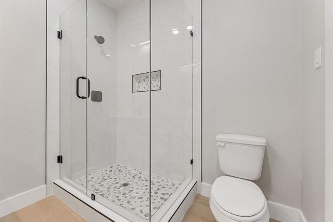 This beautifully designed walk-in shower features elegant marble-look tile, a stylish pebble stone floor, and sleek black fixtures—perfect for unwinding in a modern, tranquil space. The clean, frameless glass doors add a touch of sophistication to your primary bath. | Image 23
