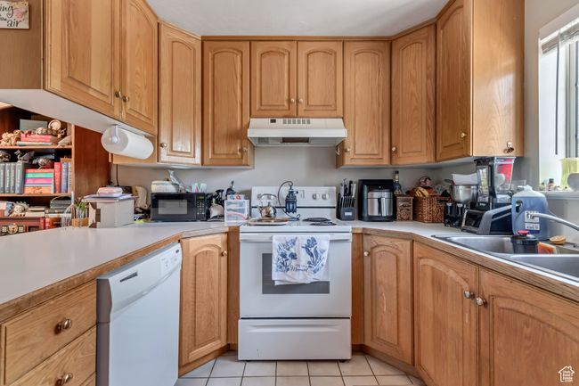 Kitchen featuring white appliances, under cabinet range hood, light countertops, and light tile patterned floors | Image 7