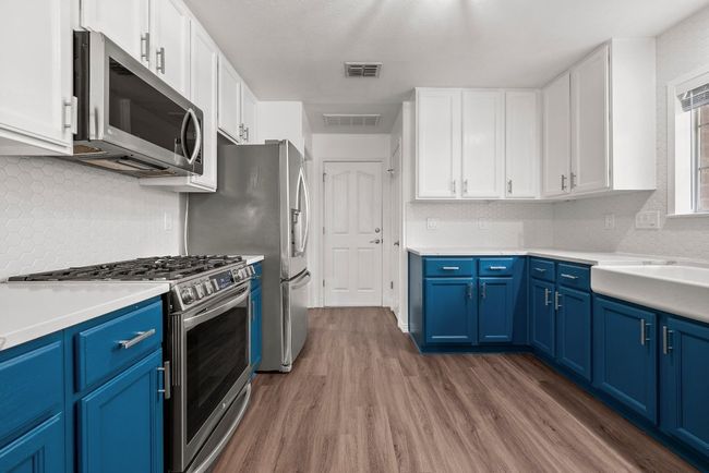 Kitchen featuring stainless steel appliances, blue cabinets, wood finished floors, and white cabinets | Image 9