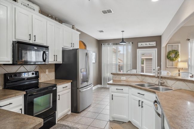 Kitchen with a sink, visible vents, white cabinets, decorative backsplash, and black appliances | Image 10
