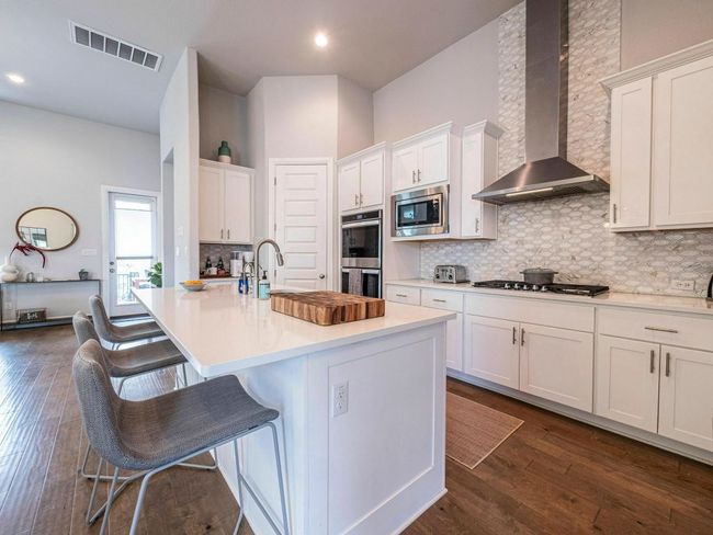 Kitchen with wall chimney exhaust hood, stainless steel appliances, white cabinetry, tasteful backsplash, and light countertops | Image 11