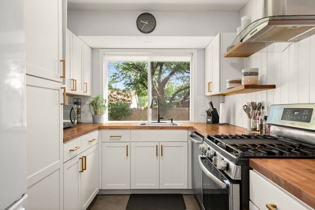 Kitchen with butcher block countertops, appliances with stainless steel finishes, a sink, ventilation hood, and white cabinets | Image 9