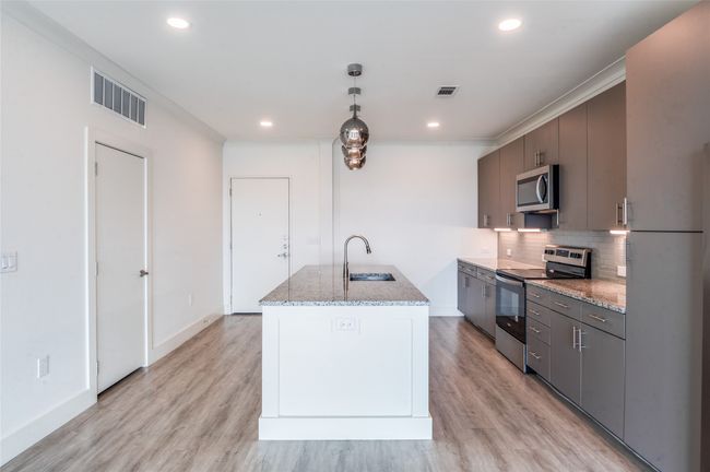 Kitchen featuring stainless steel appliances, light wood-type flooring, decorative backsplash, a center island with sink, and recessed lighting | Image 4