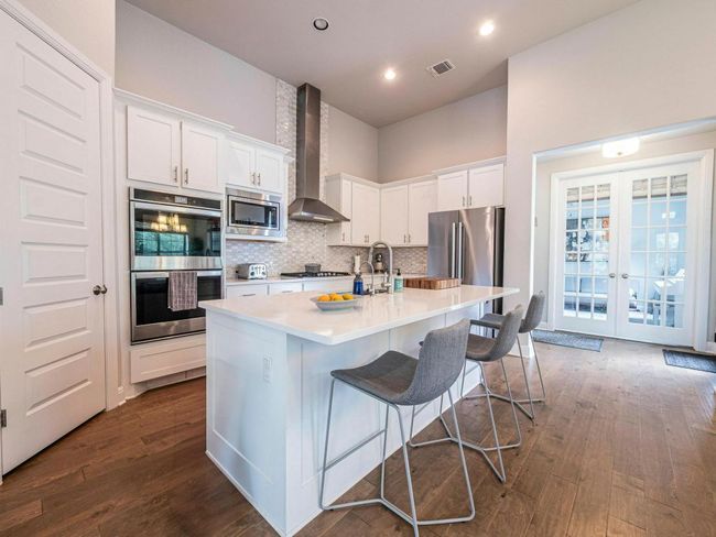 Kitchen with stainless steel appliances, wall chimney range hood, dark wood-style flooring, light countertops, and white cabinetry | Image 10