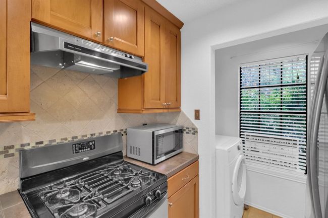 Kitchen with decorative backsplash, brown cabinets, under cabinet range hood, gas range, and washer / dryer | Image 7
