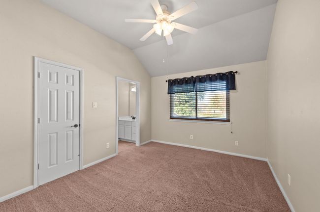 Unfurnished bedroom featuring light carpet, vaulted ceiling, ensuite bath, and a ceiling fan | Image 21