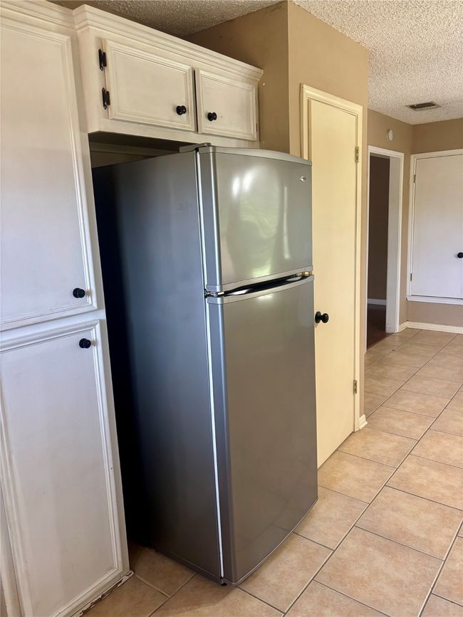 Kitchen featuring freestanding refrigerator, a textured ceiling, light tile patterned floors, and white cabinetry | Image 11