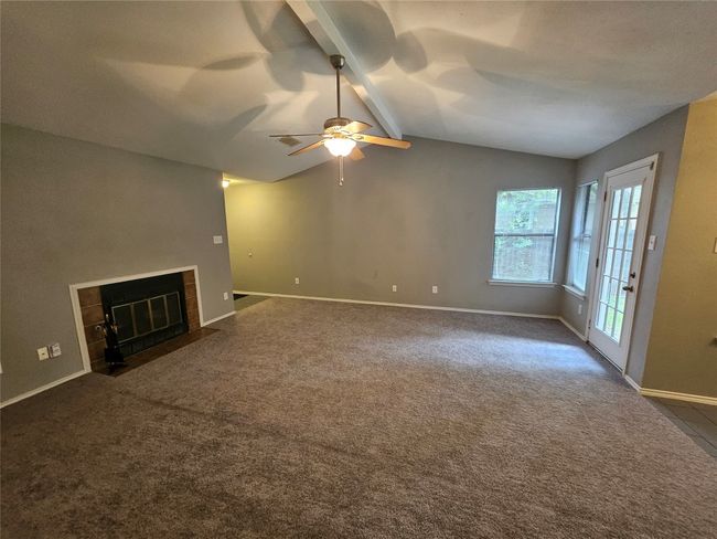Unfurnished living room featuring a tile fireplace, a ceiling fan, dark carpet, vaulted ceiling with beams, and baseboards | Image 7