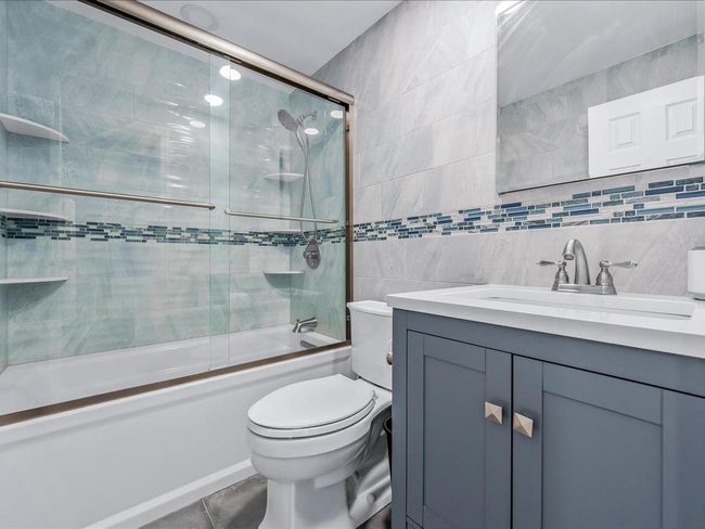 Full bathroom featuring tile walls, vanity, toilet, bath / shower combo with glass door, and tile patterned floors | Image 21