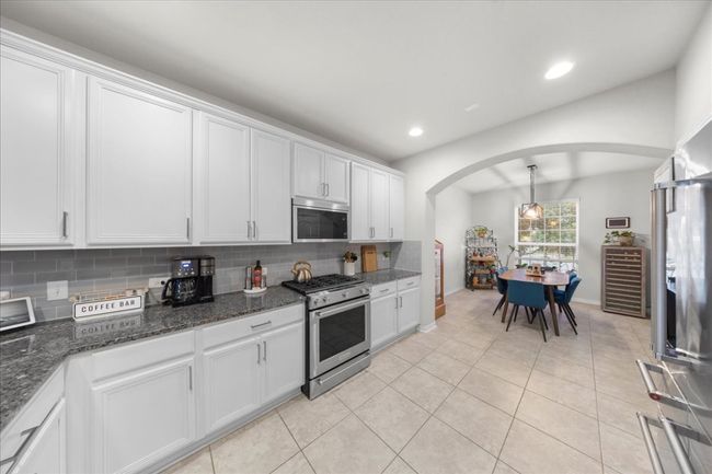 Kitchen featuring appliances with stainless steel finishes, arched walkways, beverage cooler, tasteful backsplash, and white cabinetry | Image 4