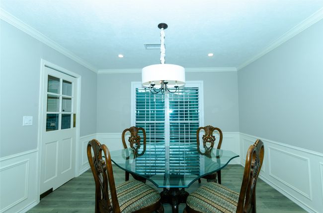 Dining space featuring wainscoting, crown molding, dark wood-style floors, a decorative wall, and a chandelier | Image 11
