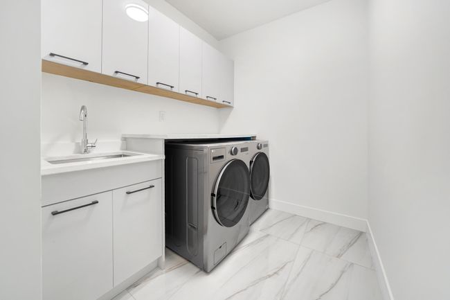 Washroom with washing machine and dryer, cabinet space, light marble finish floors, and baseboards | Image 25