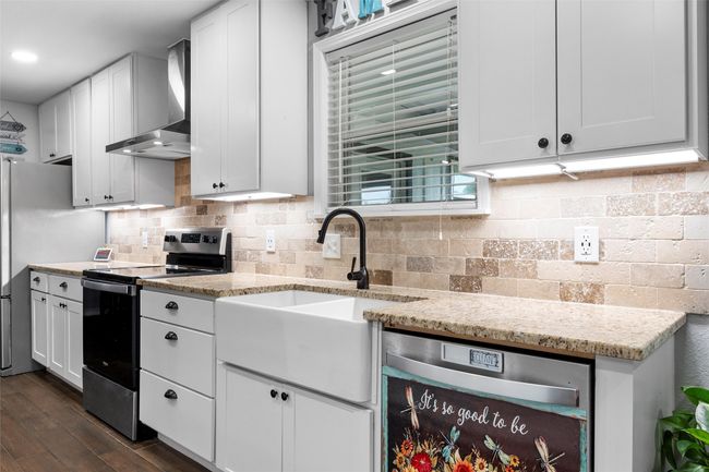 Kitchen featuring stainless steel appliances, wall chimney exhaust hood, dark wood-style flooring, white cabinets, and backsplash | Image 13
