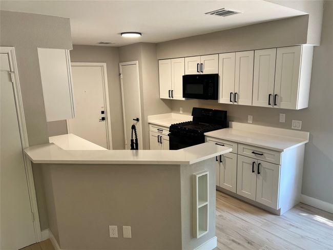 Kitchen featuring black appliances, light wood-style flooring, white cabinetry, and light countertops | Image 4