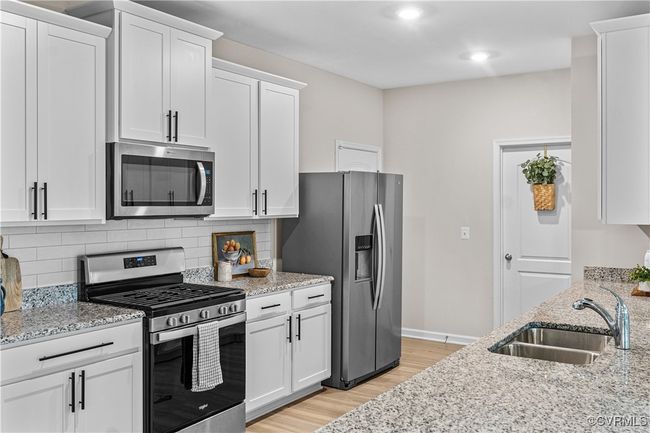 Kitchen with stainless steel appliances, a sink, light wood-style flooring, white cabinets, and backsplash | Image 15