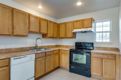 Kitchen featuring black electric range, light tile patterned floors, white dishwasher, and sink | Image 3