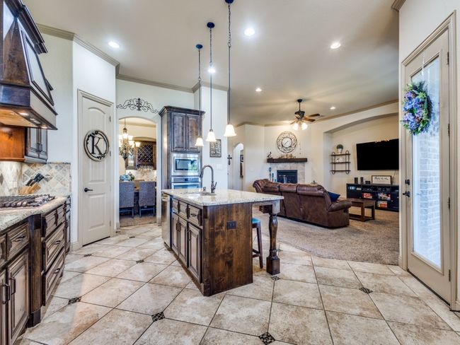 Kitchen with ornamental molding, custom exhaust hood, a chandelier, a tiled fireplace, and a ceiling fan | Image 9