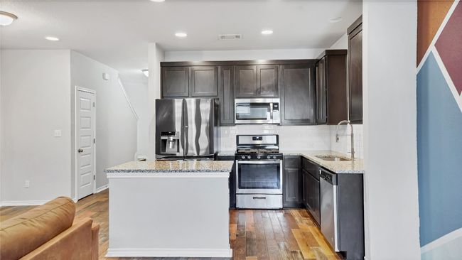 Kitchen featuring appliances with stainless steel finishes, light stone countertops, a sink, and hardwood / wood-style floors | Image 13