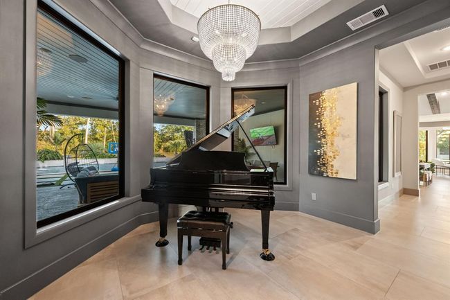 This elegant room features large windows with garden views, and a stunning chandelier. Modern art and neutral tones create a sophisticated ambiance, perfect for music and relaxation. | Image 40
