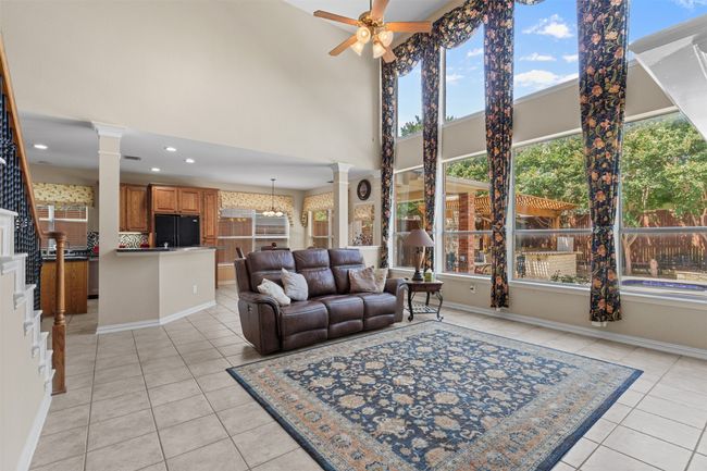 Living area with decorative columns, light tile patterned flooring, ceiling fan, a towering ceiling, and baseboards | Image 15