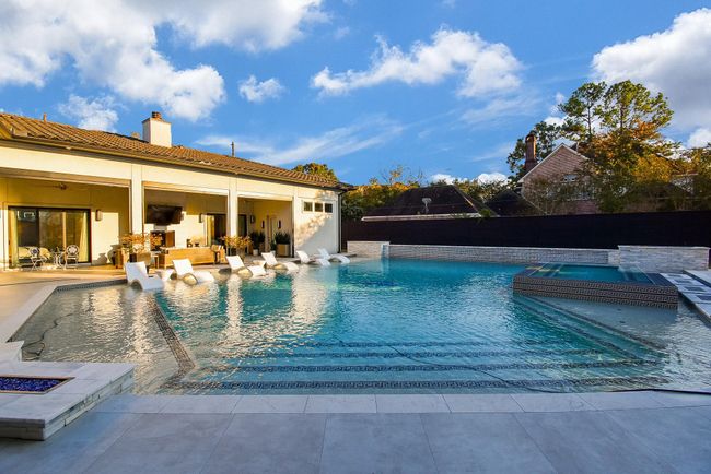 This photo showcases a luxurious backyard with a large, inviting pool + spa, surrounded by a spacious patio and a covered seating are plus fire features. | Image 45