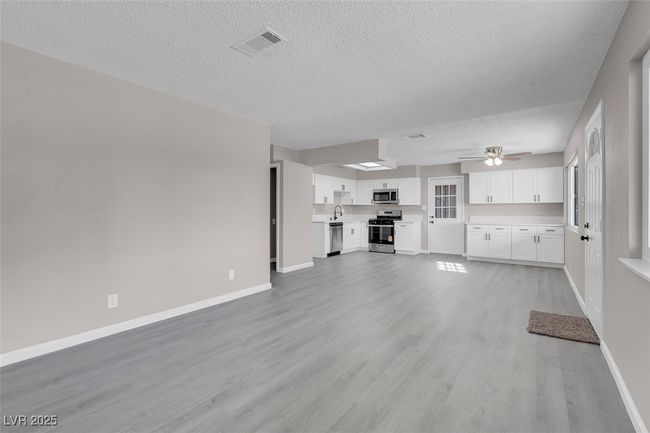 Unfurnished living room featuring light wood-style flooring, a textured ceiling, baseboards, visible vents, and a ceiling fan | Image 10