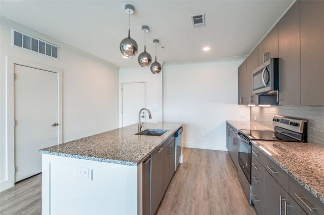 Kitchen with appliances with stainless steel finishes, light wood finished floors, tasteful backsplash, an island with sink, and recessed lighting | Image 6