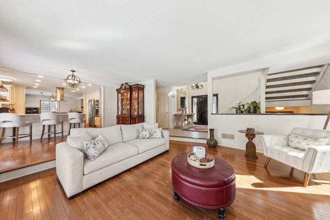 Open-concept main level featuring a cozy living room, elevated kitchen with breakfast bar seating, and seamless flow to the foyer and staircase with abundant natural light. | Image 7