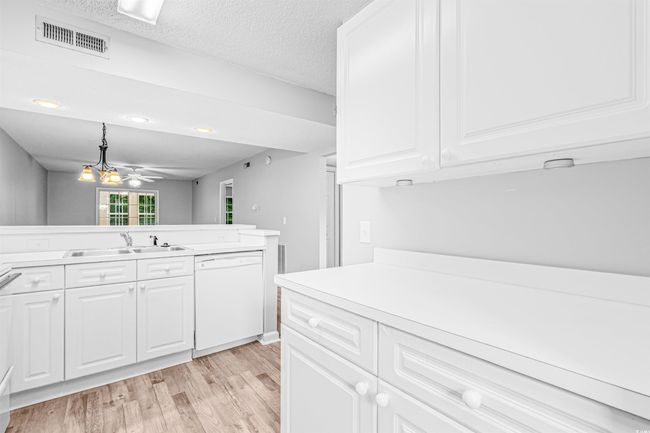 Kitchen featuring white dishwasher, light wood-style floors, light countertops, white cabinetry, and decorative light fixtures | Image 10