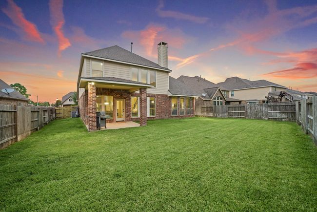 Spacious backyard with well-maintained lawn, bordered by a wooden fence for privacy. This two-story home features a covered patio, brick and siding exterior, and large windows. Perfect for outdoor activities and entertaining. | Image 40