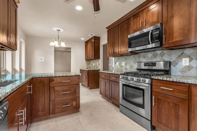 Kitchen with appliances with stainless steel finishes, backsplash, light stone counters, ceiling fan, and light tile patterned floors | Image 8