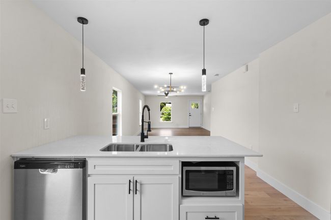 Kitchen featuring appliances with stainless steel finishes, a peninsula, white cabinetry, light wood-style floors, and hanging light fixtures | Image 17