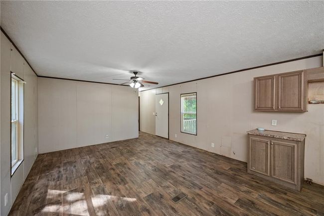 Unfurnished living room featuring dark wood-style floors, a ceiling fan, a textured ceiling, and crown molding | Image 14