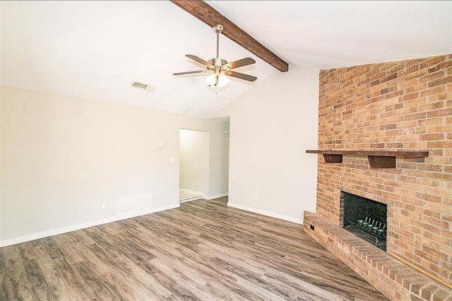 Unfurnished living room with a ceiling fan, wood finished floors, and a fireplace | Image 4
