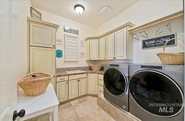 Laundry area with cabinet space, washing machine and clothes dryer, light tile patterned floors, and a textured ceiling | Image 28