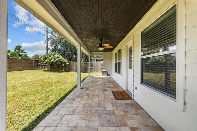 A covered patio with tile flooring and a ceiling fan, overlooking a spacious, fenced backyard. It's perfect for outdoor relaxation and entertaining. | Image 43
