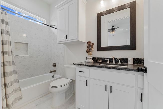 Bathroom with marble finish floor, ceiling fan, toilet, vanity, and shower / bath combination with curtain | Image 5
